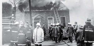 Structural Fire Training in Washington in the 1970’s. Buildings donated by local residents to be burned for training purposes were not uncommon, before several thousand pages of rules were developed by the EPA. Fire Chief Don Hahne is in the foreground of the photo in the white gear and Instructor Westhoff is in the white helmet at the right corner of the structure. A great time was had by all.